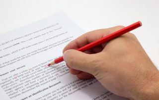 Hand holding a red pen proofreading and copyediting documents