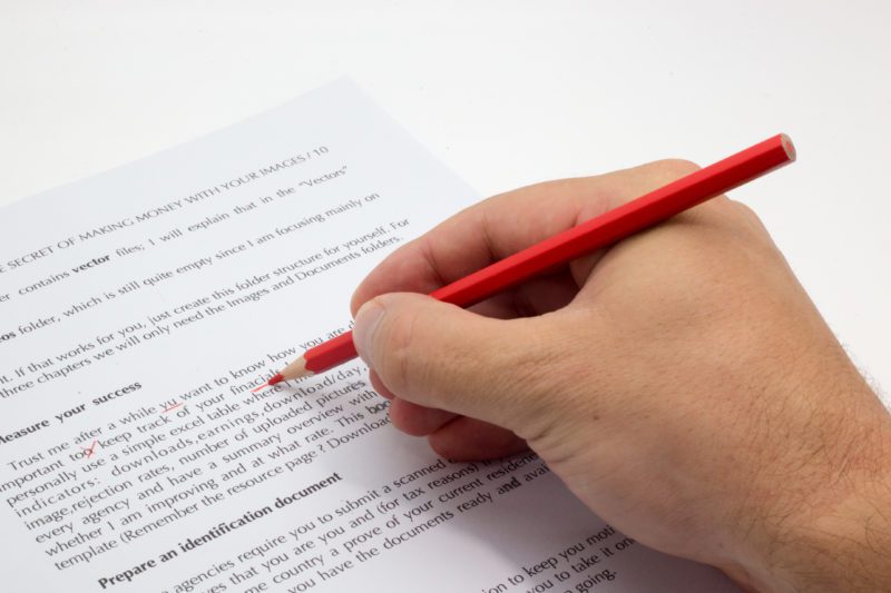 Proofreading vs. copyediting. Hand holding a red pen proofreading and copyediting documents