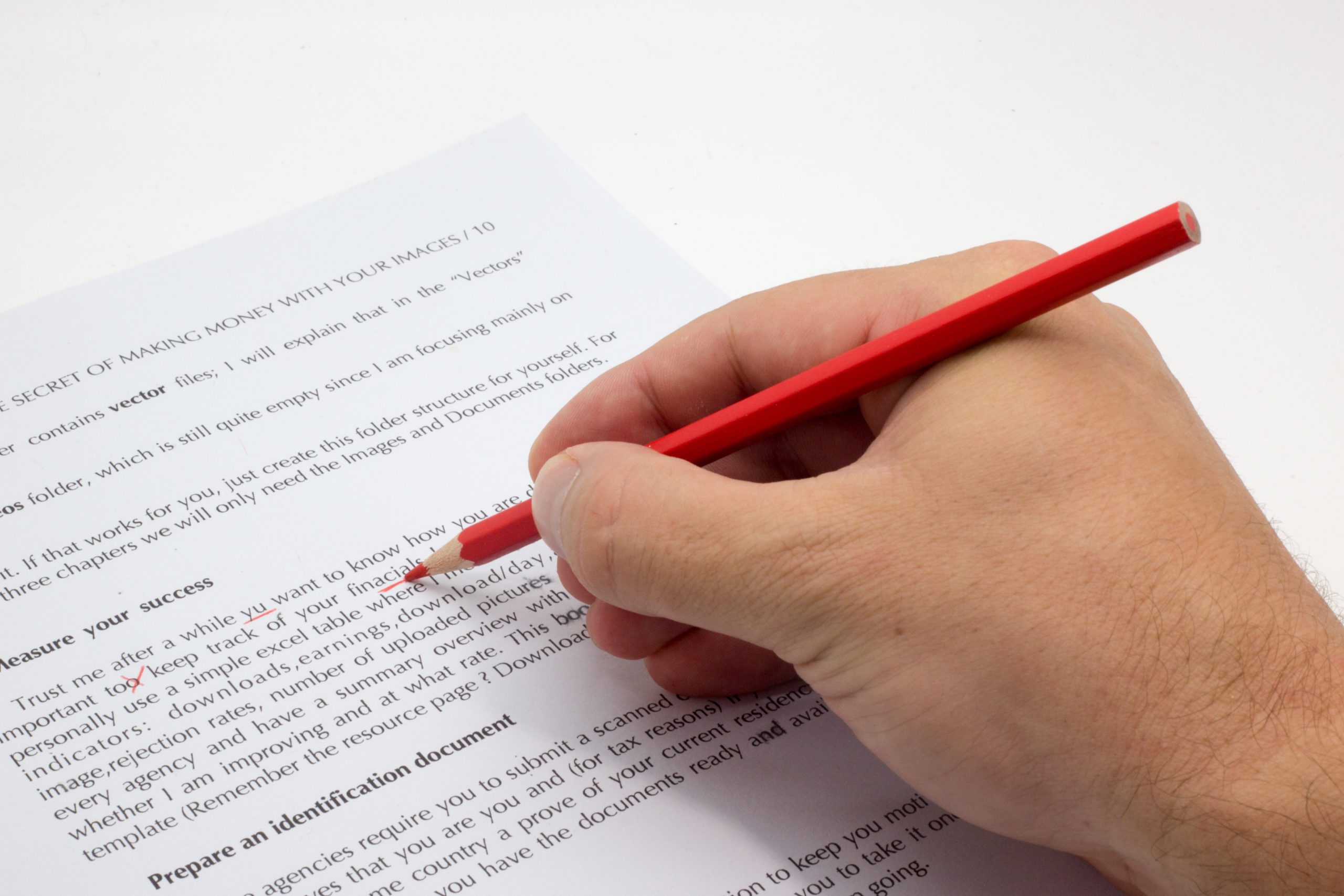 Hand holding a red pen proofreading and copyediting documents