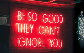 A red neon sign saying the phrase 'be so good they can't ignore you'.