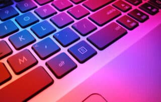 Image shows a close up of a laptop keyboard bathed in pink light.